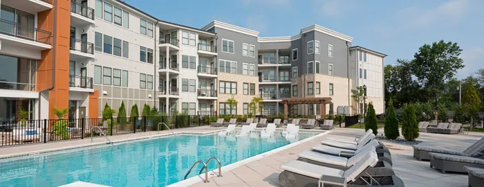 Modern apartment complex with a luxurious poolside area, surrounded by comfortable loungers and lush greenery, offering a serene and stylish living environment.
