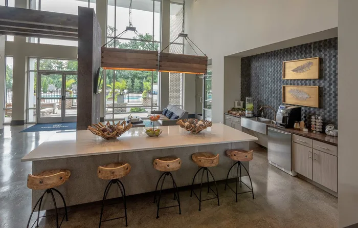 Bright open-concept lounge area with modern kitchen, stylish wooden bar stools, and large windows showcasing a pool view.