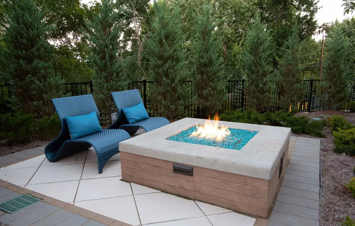 Tranquil outdoor patio with modern fire pit and stylish lounge chairs, surrounded by lush greenery.