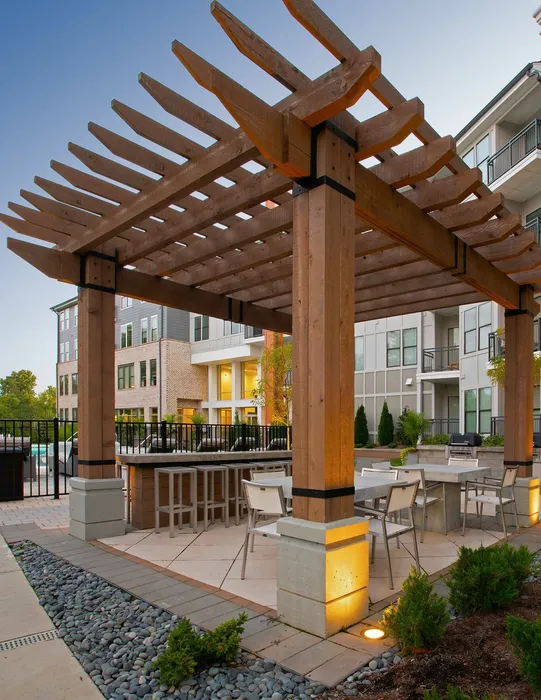 Charming outdoor patio with modern pergola, stylish seating, and lush greenery, perfect for relaxing in a vibrant apartment community.