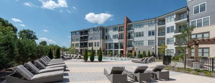 Modern apartment complex with sleek architecture, surrounded by lush greenery and a vibrant courtyard featuring stylish lounge chairs.
