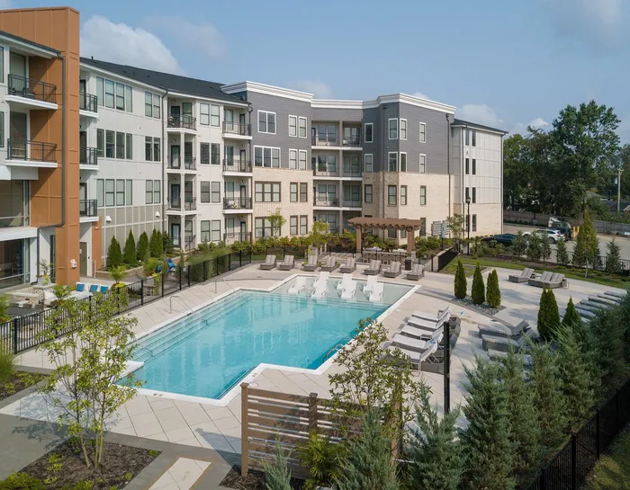 Contemporary apartment complex with luxurious outdoor pool and lounge area, surrounded by lush landscaping and modern architecture.