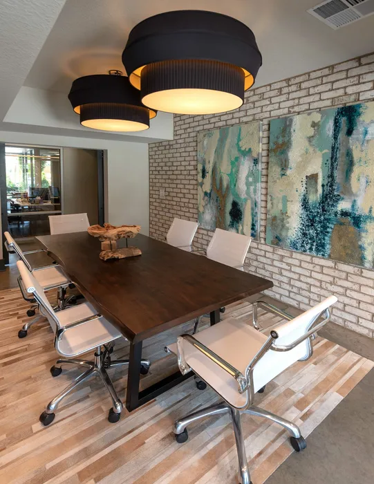 Chic meeting room with a modern wooden table, sleek white chairs, and artistic wall decor, enhanced by stylish overhead lighting.
