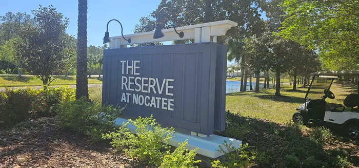 Inviting entrance sign at The Reserve at Nocatee, surrounded by lush greenery and scenic landscaping with a charming pond view.