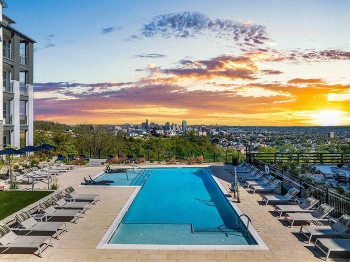 Luxurious apartment complex pool with panoramic city skyline views and stunning sunset backdrop.