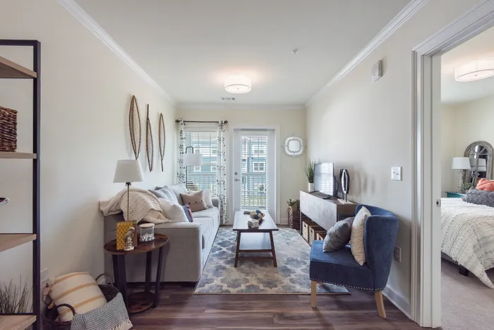 Charming living room with cozy sofa, elegant decor, and natural light from large windows, leading to a serene bedroom retreat.