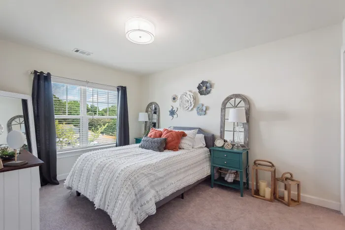 Bright bedroom with chic decor, featuring elegant wall art, stylish bedside tables, and a large window with tree views.