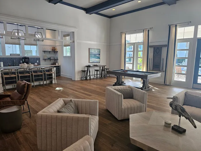 Elegant living area featuring a modern kitchen with bar stools, a stylish billiard table, chic seating, and large windows inviting natural light.