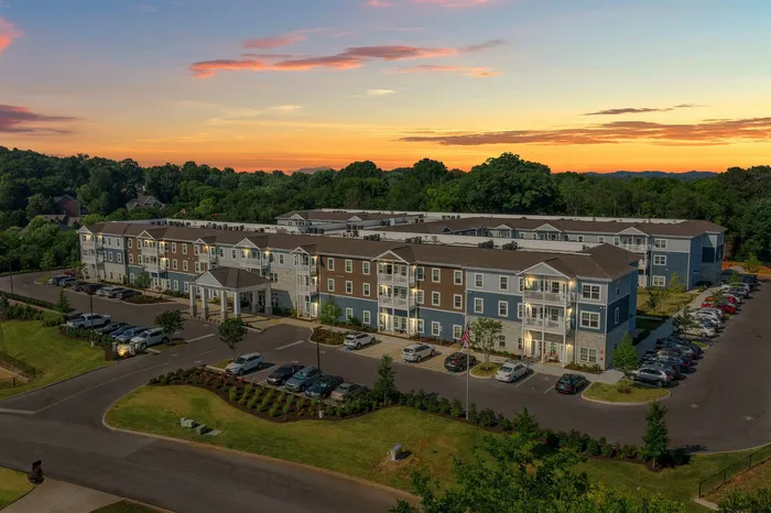 Charming apartment complex at sunset surrounded by lush greenery, featuring modern architecture and ample parking.