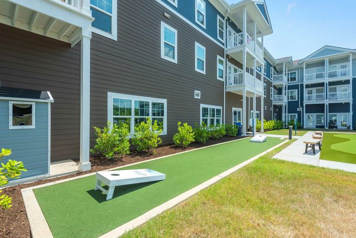 Charming apartment complex with a vibrant lawn area featuring a fun outdoor game setup and inviting benches for relaxation.