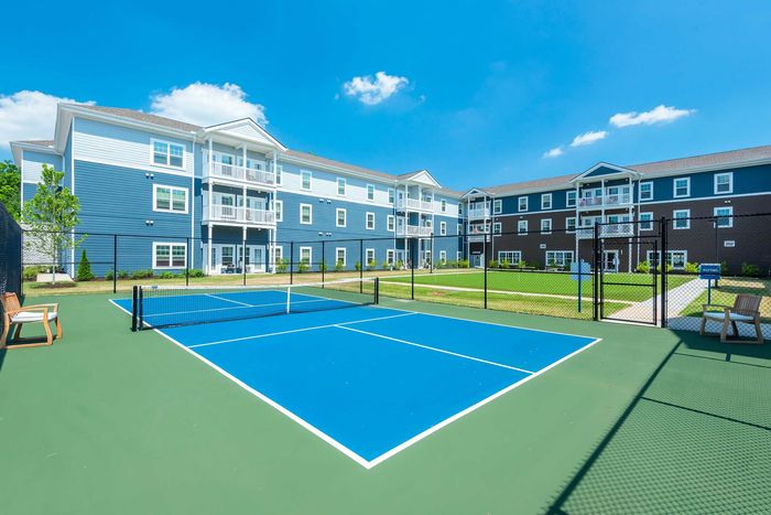 Modern apartment community featuring stylish buildings and a vibrant tennis court under a clear blue sky.