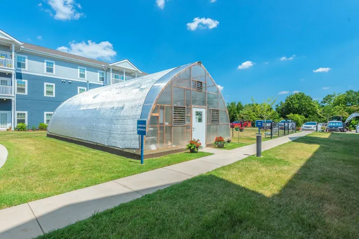 Charming apartment complex featuring a modern hydroponic greenhouse nestled in a lush green lawn, perfect for sustainable living enthusiasts.