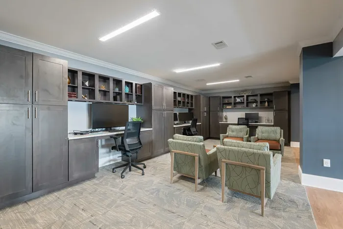 Modern home office with sleek dark wood cabinets, dual workstations, and cozy seating area.