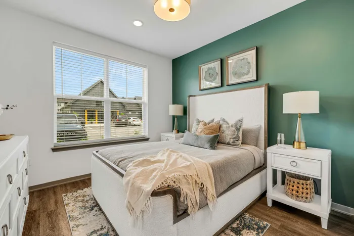 Cozy bedroom with elegant decor, featuring a plush bed and stylish accents, complemented by a soothing green accent wall and natural light streaming through large windows.