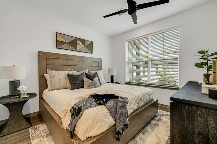 Inviting bedroom featuring a plush bed with stylish pillows, a modern ceiling fan, and abundant natural light from large windows.
