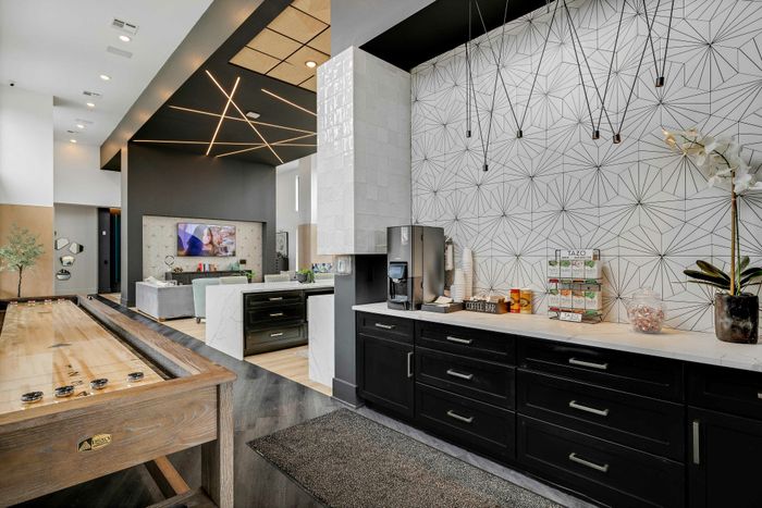 Modern communal lounge with sleek geometric design, shuffleboard table, and a chic coffee bar area.