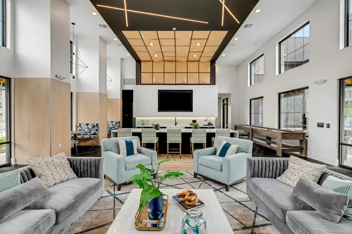Sleek, modern living area featuring stylish sofas, accent chairs, a large flat-screen TV, and a contemporary ceiling design.