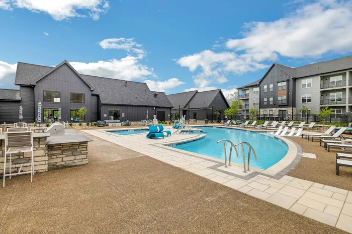 Luxurious apartment complex featuring a sparkling outdoor pool, modern lounges, and sun deck under a vibrant blue sky.