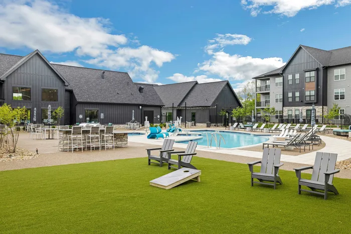 Inviting modern apartment complex with a sparkling outdoor pool, elegant lounge chairs, and pristine landscaping under a bright blue sky.