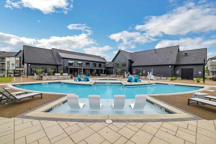 Luxurious apartment complex pool area with elegant lounging chairs, surrounded by modern architecture and vibrant blue sky.