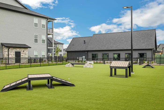 Inviting dog park with agility equipment and modern apartments in the background, perfect for pet-friendly living.