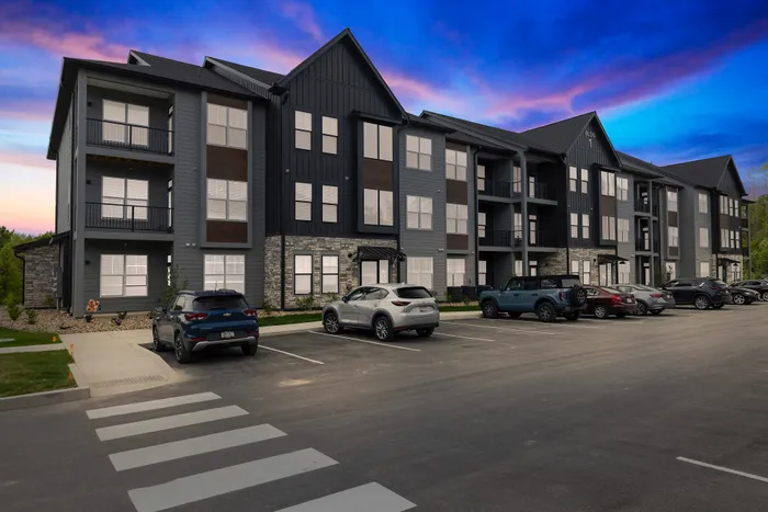 Contemporary apartment complex with elegant facade, ample parking, and serene sunset backdrop.