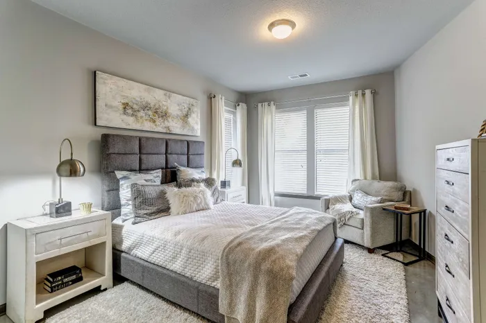 Inviting bedroom with modern decor, featuring a plush bed, abstract artwork, and natural light streaming through large windows.