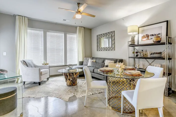 Chic and inviting living room with modern decor, featuring a cozy gray sofa, glass and wood coffee table, and stylish dining area with elegant chairs.