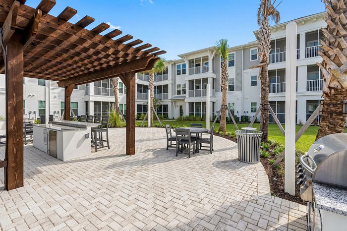 Inviting outdoor courtyard with a modern pergola, stylish seating areas, and lush landscaping, perfect for relaxation and gatherings in front of elegant apartment buildings.