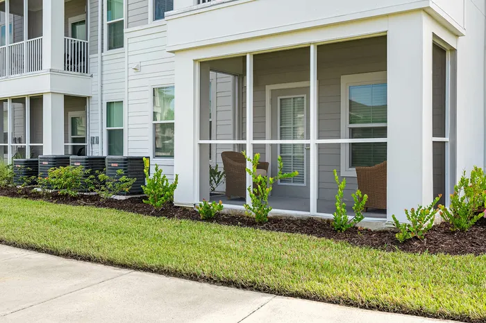 Charming apartment exterior with screened-in porch, cozy seating area, and well-maintained landscaping for relaxing outdoor moments.