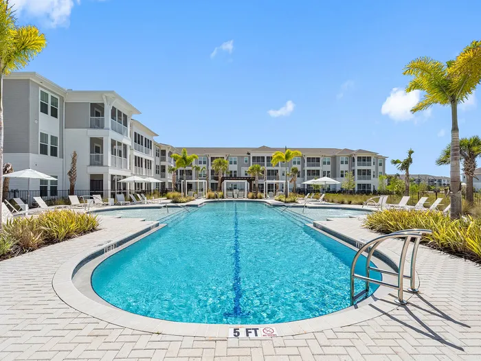 Luxurious apartment complex featuring a sparkling outdoor pool with palm trees and sun loungers, perfect for relaxation.