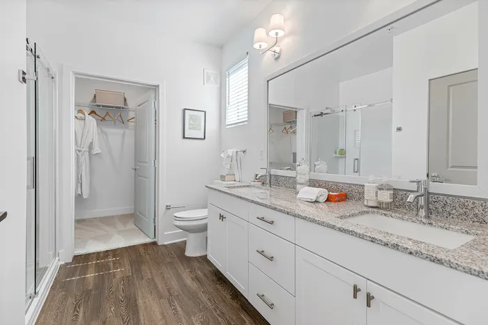 Elegant bathroom with modern granite countertops, stylish double vanity, and spacious walk-in closet featuring plush robes.