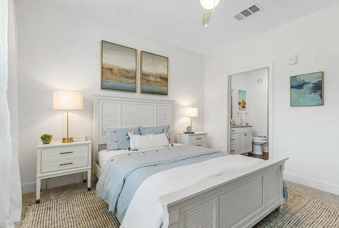 Elegant bedroom with modern d&eacute;cor, featuring a cozy bed with blue bedding, stylish lamps, and framed artwork, leading to an en-suite bathroom.