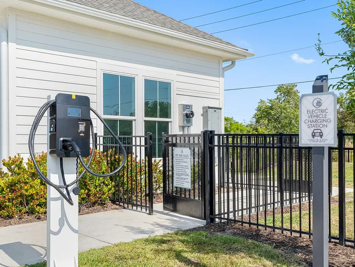 Modern electric vehicle charging station outside a stylish residential building, featuring white siding and lush greenery.