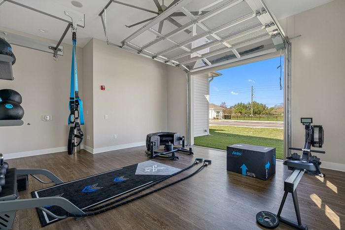 Modern home gym with stylish equipment, expansive open garage door revealing lush greenery outside.