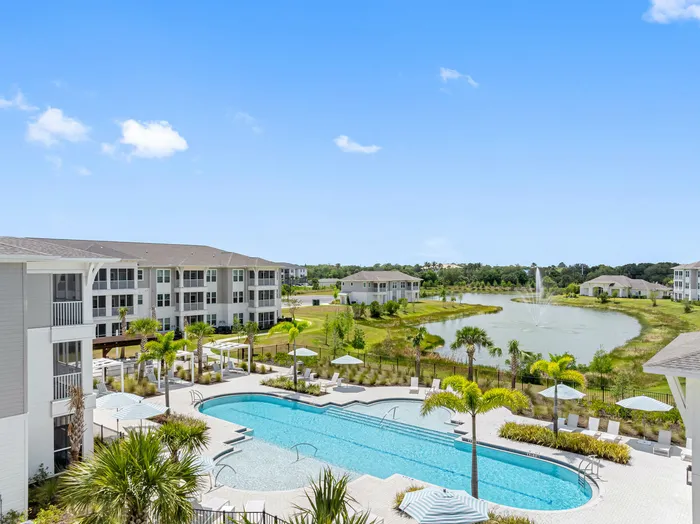 Luxurious apartment complex with a sparkling pool, surrounded by lush greenery and a serene pond with a fountain.