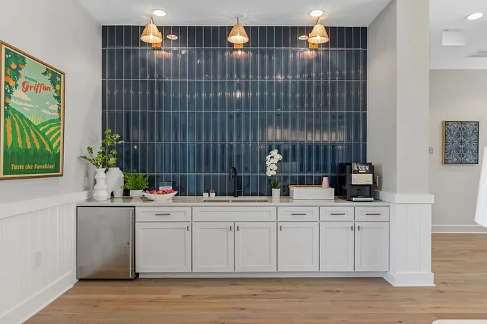 Chic kitchenette boasting sleek white cabinets, elegant blue tiled backsplash, and modern lighting fixtures, exuding contemporary charm.