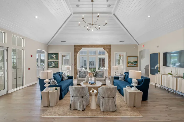 Elegant living room with vaulted ceiling, featuring plush blue sofas, stylish armchairs, and natural light streaming through large windows.