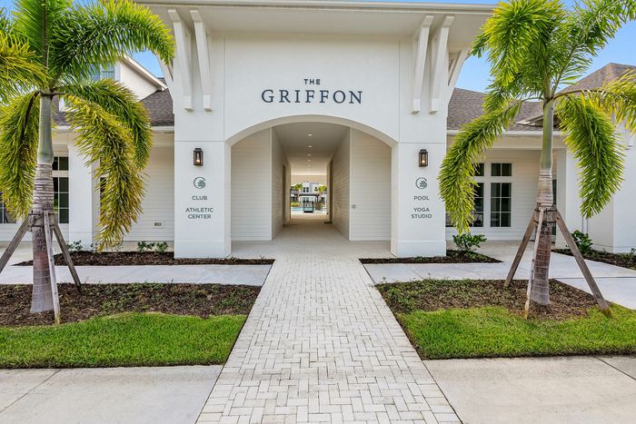 Entrance to The Griffon, showcasing elegant architecture, lush palm trees, and amenities like a pool, yoga studio, and athletic center.