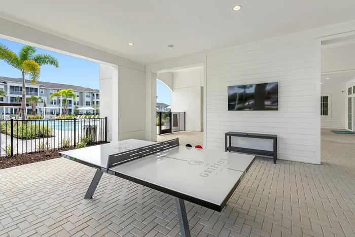 Inviting outdoor recreation area featuring a sleek ping pong table, scenic pool view, and lush palm trees, perfect for leisure and entertainment.