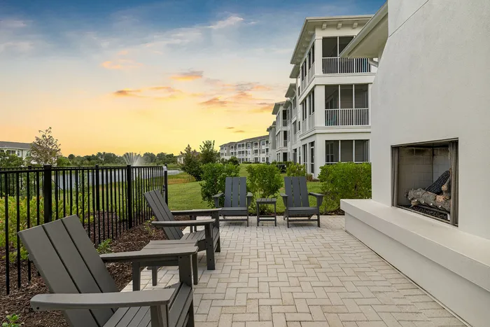 Charming outdoor patio featuring cozy seating and a modern fireplace, with picturesque views of a fountain and lush landscaping at sunset.