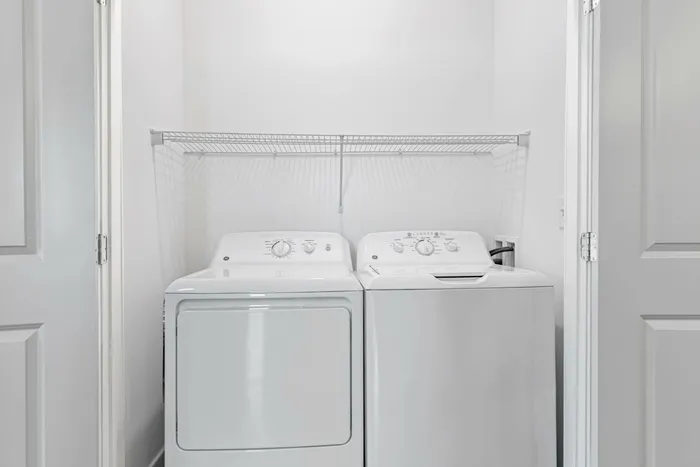 Bright, modern laundry nook featuring a sleek washer and dryer with convenient shelving above.
