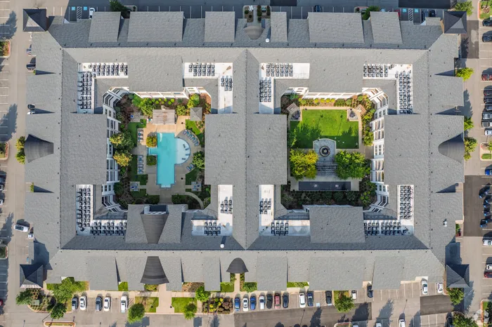 Arial view of a luxury apartment complex featuring a central swimming pool, lush gardens, and ample outdoor seating areas.