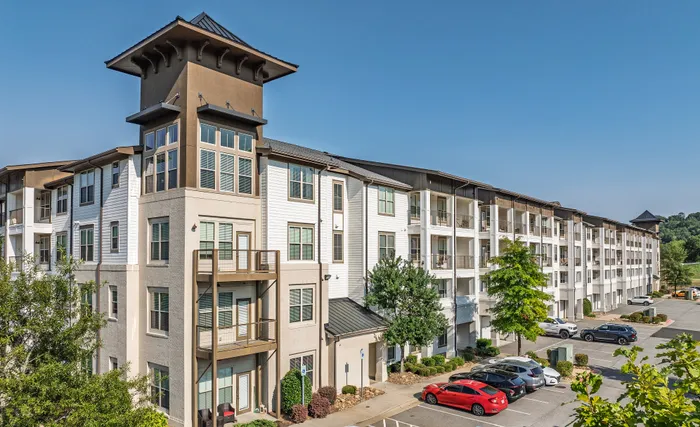 Elegant apartment building exterior showcasing modern architecture, spacious balconies, and ample parking, surrounded by lush greenery.