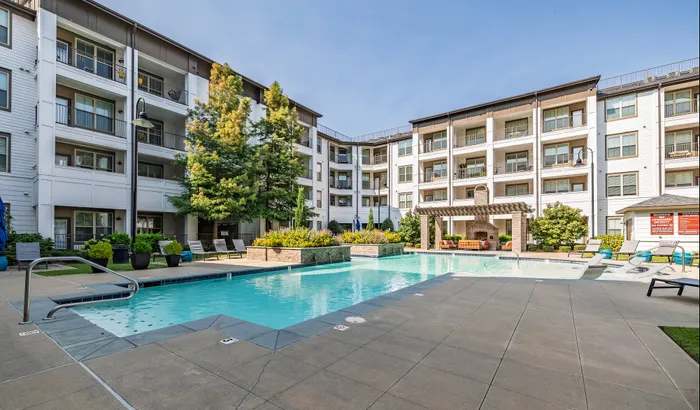 Luxurious apartment complex with a sparkling pool, surrounded by lush greenery and stylish lounging areas, perfect for relaxation and leisure.