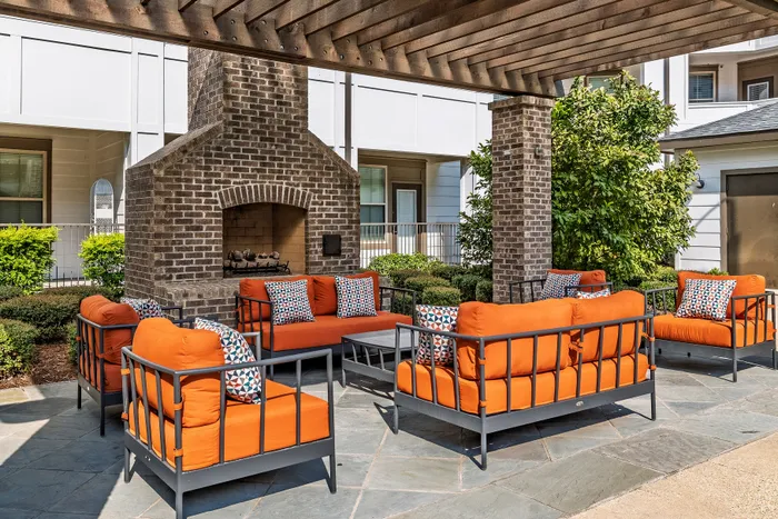 Inviting outdoor seating area with vibrant orange cushions, accentuated by a rustic brick fireplace and lush greenery.