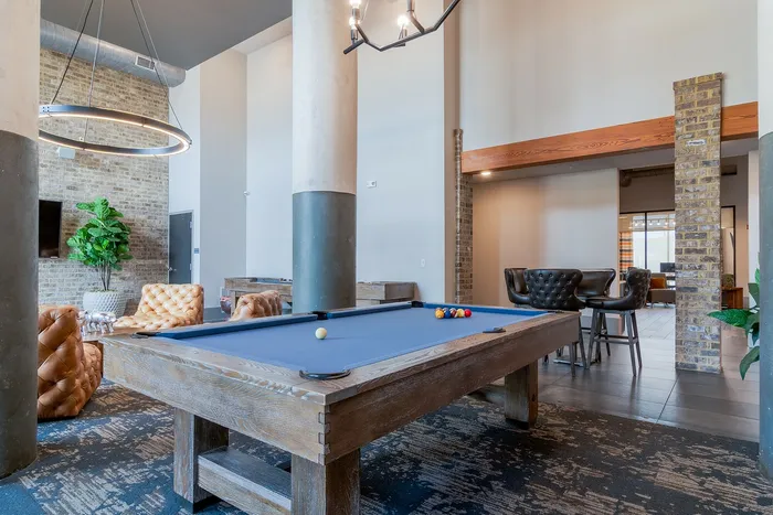 Chic communal lounge with a stylish pool table, plush leather seating, modern lighting, and exposed brick accents, perfect for socializing and relaxation.