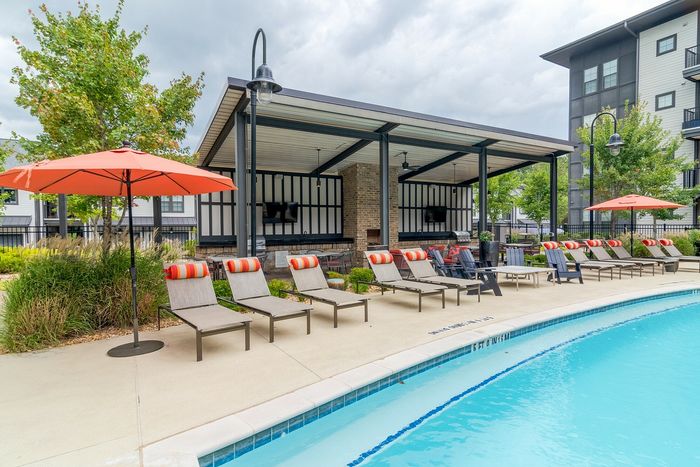 Inviting outdoor pool area with stylish lounge chairs and vibrant orange umbrellas, perfect for relaxing under the sun.