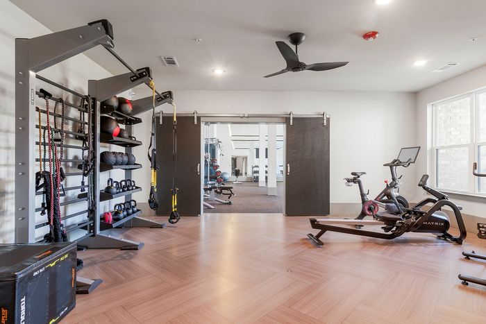 Modern fitness room with well-equipped workout stations featuring exercise bikes, kettlebells, and resistance bands on elegant wood flooring.