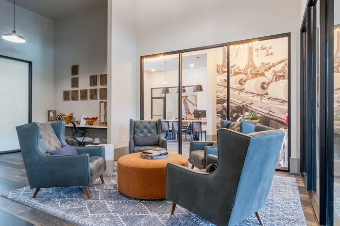 Inviting modern lounge area with plush blue chairs and a cozy round ottoman, perfect for relaxation and social gatherings in a stylish setting.